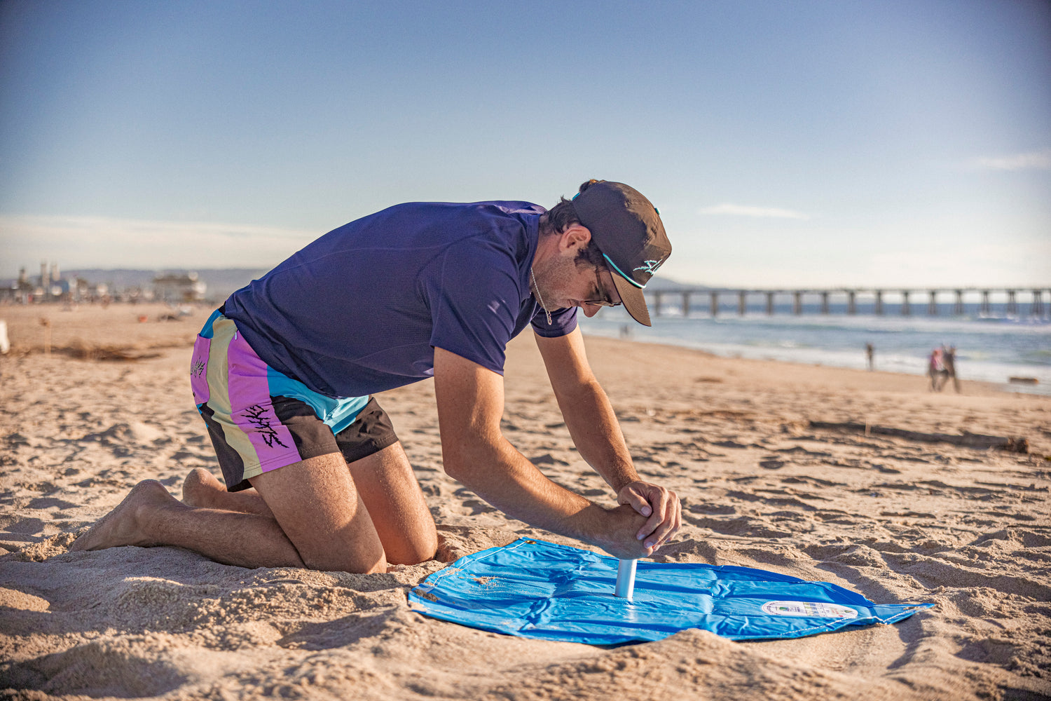 man using sand digger tool at beach to dig a hole for beach umbrell