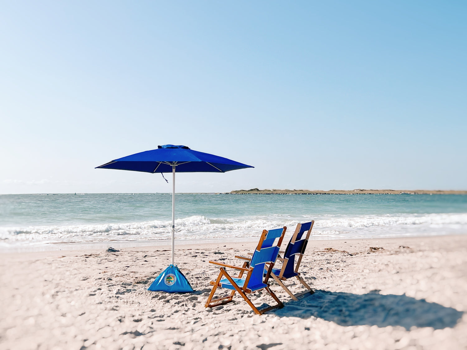 premium wind resistant beach umbrella set up at the beach with two lounge chairs