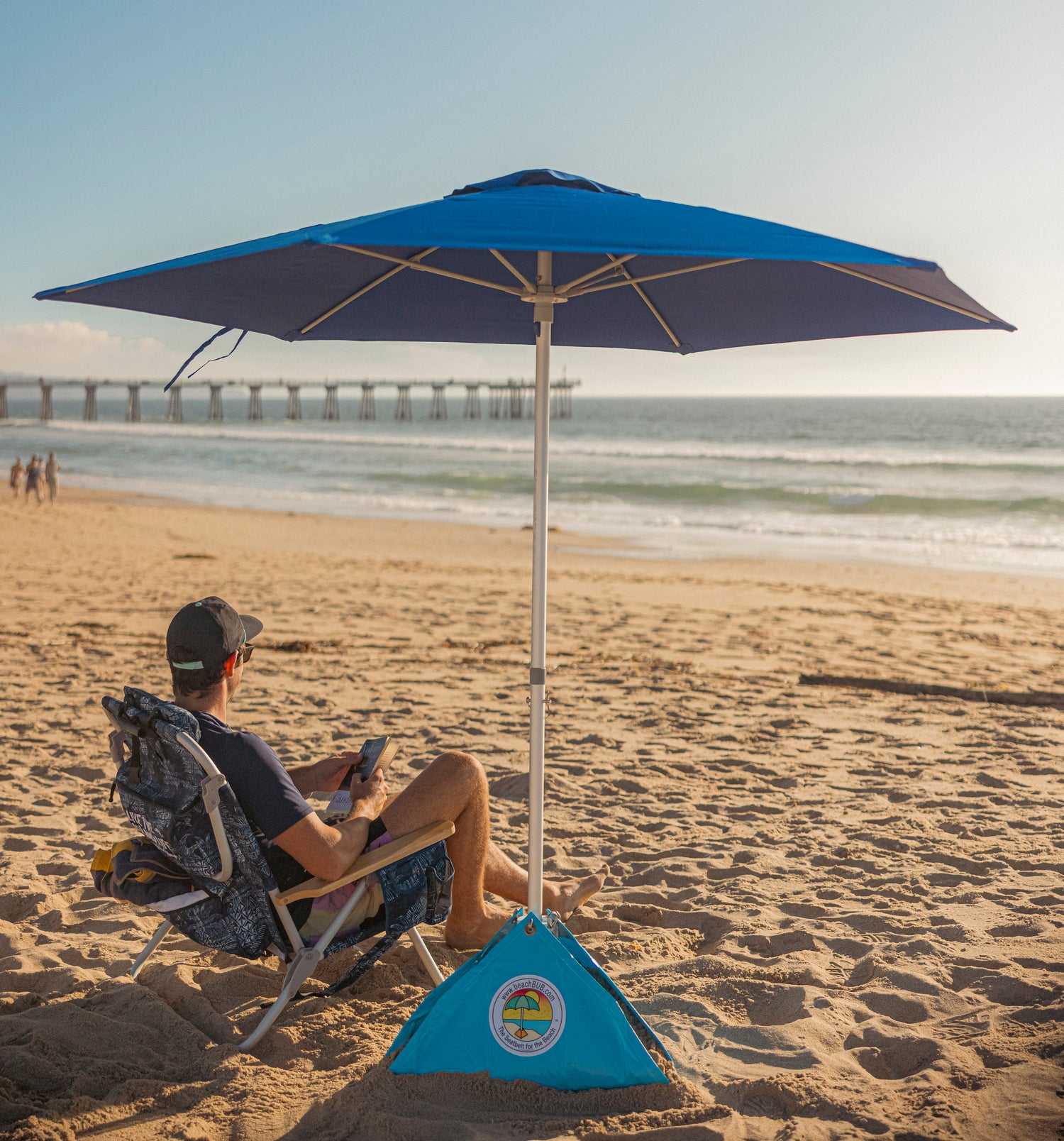 man relaxing at the beach underneath a blue wind resistant beach umbrella